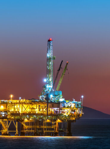 Offshore oil platform off the coast of California against a moody, orange sky as the sun sets behind the rig.