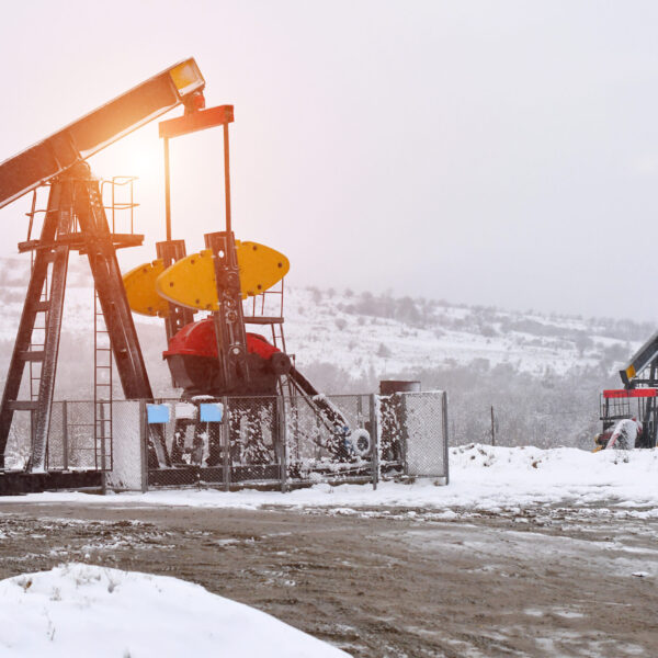 Oil pump. Oil and gas industry equipment. Oil field pump jack and oil refinery in the winter with snow, mountains,  
forest and sunset in background